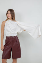 Load image into Gallery viewer, Woman wearing an ivory satin one-shoulder asymmetrical blouse with draped scarf detail paired with burgundy leather pants
