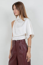 Load image into Gallery viewer, Woman wearing an ivory satin one-shoulder asymmetrical blouse with draped scarf detail paired with burgundy leather pants
