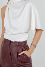 Load image into Gallery viewer, Woman wearing an ivory satin one-shoulder asymmetrical blouse with draped scarf detail paired with burgundy leather pants
