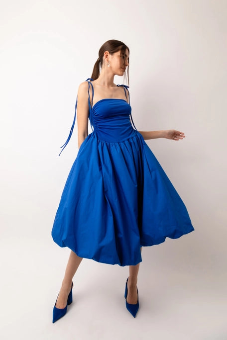 A stunning strapless midi dress with stretch fitted bodice and a full cotton skirt. Drawstring tie details either side of the bodice to create a slight ruched effect. The skirt is fully lined and has a classic puff ball effect. Dress it up or down! 