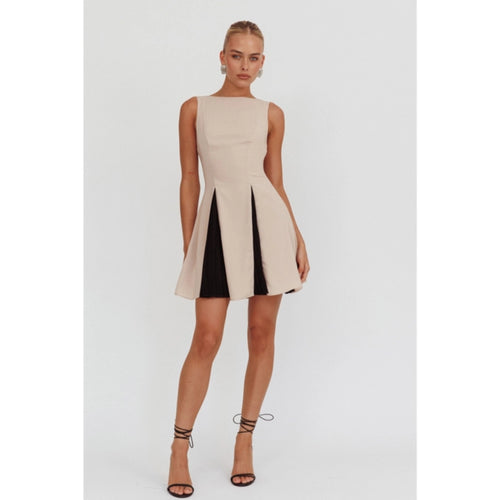 A sleeveless beige mini dress featuring a boat neckline and contrast black accents peeking through the pleats, creating a chic and versatile look suitable for any occasion. 