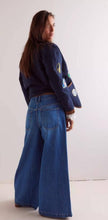 Load image into Gallery viewer, Person wearing a dark jacket with patches and blue wide leg jeans against a white background
