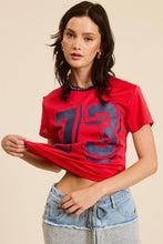 Load image into Gallery viewer, Unleash your sporty side with our Crop Jersey Tee Number 73! This baby tee blends comfort and style, featuring a soft jersey fabric that hugs your body just right. The bold number 73 adds a touch of athletic flair, making it perfect for casual outings or an active day out. Pair it with high-waisted jeans or your favorite shorts for a trendy, effortless look. Elevate your wardrobe with this must-have sporty staple!
