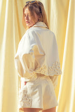 Load image into Gallery viewer, Model wearing écru tailored shorts with oversized floral appliqué embroidery paired with coordinating top in a soft neutral ivory/yellow tone.
