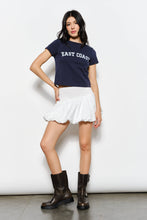 Load image into Gallery viewer, Woman wearing a navy blue &#39;East Coast&#39; t-shirt, white skirt, and black boots on a white background
