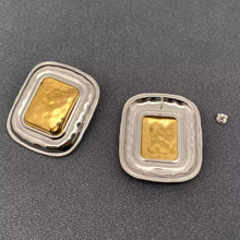 Load image into Gallery viewer, Pair of oversized two-tone statement earrings featuring sculptural rounded rectangular silver-tone frames and raised polished gold-tone centers.

