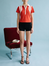 Load image into Gallery viewer, Red short-sleeve polo top with white contrast collar and panel detailing, styled with black shorts for a sporty chic look.
