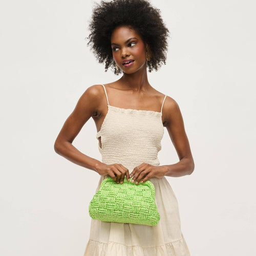 Woman holding a green woven clutch bag against a plain background.