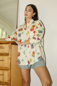 Cream-colored button-up shirt with colorful grocery and snack print, featuring short sleeves and a relaxed fit - perfect for playful summer style. Matching printed shorts sold separately. Fun, foodie-inspired fashion exclusively at Glam Expressway.