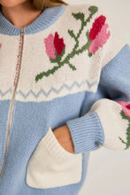 Load image into Gallery viewer, A light blue and cream color-block cardigan sweater featuring a vibrant floral intarsia knit design, seamlessly blending the comfort of a sweater with the structure of a cardigan jacket for effortless style. 
