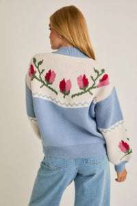 A light blue and cream color-block cardigan sweater featuring a vibrant floral intarsia knit design, seamlessly blending the comfort of a sweater with the structure of a cardigan jacket for effortless style. 