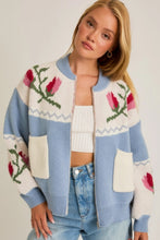 Load image into Gallery viewer, A light blue and cream color-block cardigan sweater featuring a vibrant floral intarsia knit design, seamlessly blending the comfort of a sweater with the structure of a cardigan jacket for effortless style. 
