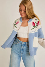 Load image into Gallery viewer, A light blue and cream color-block cardigan sweater featuring a vibrant floral intarsia knit design, seamlessly blending the comfort of a sweater with the structure of a cardigan jacket for effortless style. 
