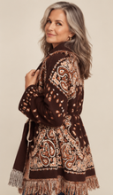 Load image into Gallery viewer, Model wearing a chocolate brown tapestry fringe cardigan with a self-tie waist belt and cream trousers.
