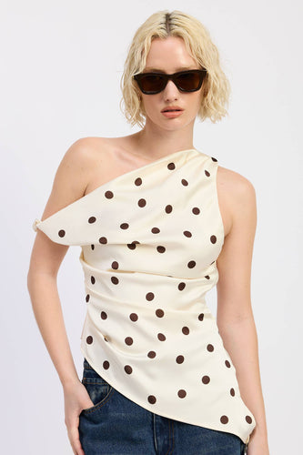 Woman wearing a one-shoulder polka dot top and sunglasses on a white background
