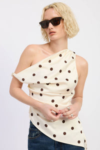 Woman wearing a polka dot one-shoulder top and sunglasses on a plain background