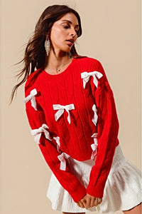 Add a playful pop of color to your wardrobe with our Cherry Red Cable Knit Sweater, adorned with delicate white ribbon bow appliqués! This cozy yet statement-making sweater features a classic cable knit design in a bold red hue, with charming white bows adding a whimsical touch. Perfect for pairing with jeans or a skirt, this sweater will keep you warm and stylish all season long. Available in sizes S to XL for the perfect fit!