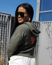 Load image into Gallery viewer, This is luxury loungewear! Our Army Green Cropped Hoodie is extremely soft and incredible quality. This stylish hoodie was designed specifically for our store with a metallic orange bird in flight on the front and a distressed hem at the waist. Made exclusively by Craig Anthony Miller for Glam Expressway! sizes come in Small - XL. Dress it up or down!
