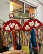 Load image into Gallery viewer, Our Heart Rainbow Earrings are outrageously stunning! These rainbows drip crystal tassels on either side making these statement earrings stand out in a crowd. The Heart Rainbow Earrings are red and pink, very light weight, have a post closure and measure 3.5&quot; x 2.&quot; Wear these stunning rainbow earrings when you want to be seen!
